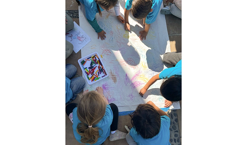 view from above of several kids working with crayons on a big piece of paper